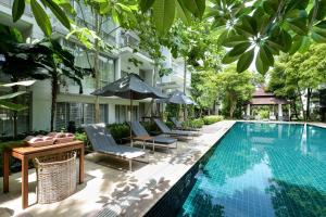 einen Pool mit Stühlen und Sonnenschirmen neben einem Gebäude in der Unterkunft The Park Nine Hotel Srinakarin in Bangkok