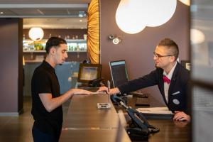 zwei Männer stehen an einem Schalter in einem Büro in der Unterkunft Hotel-Restaurant Horizon Ath-Lessines in Ghislenghien