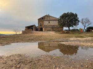 an old building on a hill with a reflection in a puddle at Masia Manonelles in Biosca