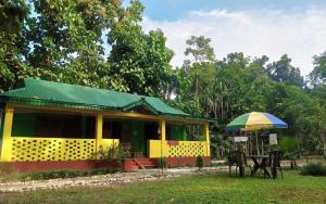 a yellow and green house with a table and an umbrella at Leo Jungle Retreat by StayApart , Jaldapara in Mādāri Hāt