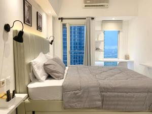 a white bedroom with a large bed and a window at Pakuwon Mall Dovey Apartment in Surabaya