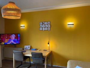 a dining room with a table and a tv on a yellow wall at Plato by Hofstad Studio’s in Scheveningen