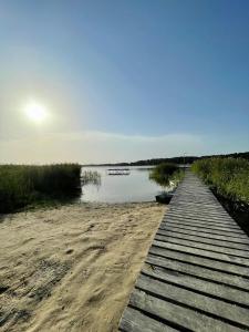 a wooden boardwalk on a beach next to a body of water at Domki pod mazurskim niebem in Pilchy