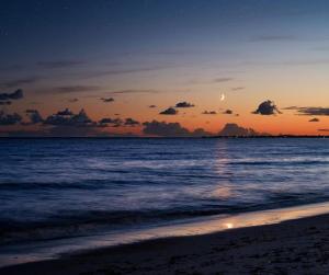 Doga Resort - דוגה ריזורט في Kinar: غروب الشمس على الشاطئ مع القمر في السماء