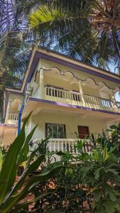 a white house with a balcony and palm trees at Santana Guest House in Agonda