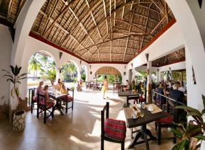 a restaurant with tables and people sitting at tables at Mambo Ocean Resort in Pwani Mchangani