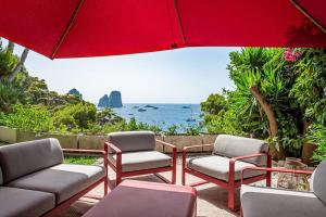 un patio con sedie, ombrellone rosso e oceano di Villa Cisterna Capri, private beach front property with pool a Capri