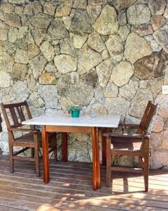 a wooden table and two chairs in front of a stone wall at Camburi Beach House - Casa térrea a 50 m da praia in São Sebastião