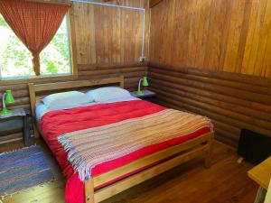 1 dormitorio con 1 cama con edredón rojo y ventana en Parador Darwin en Cucao
