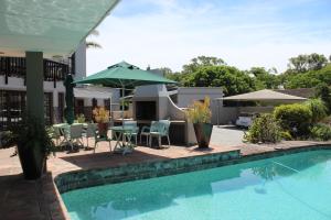a swimming pool with a table and an umbrella at Sir Roys Guest House in Port Elizabeth