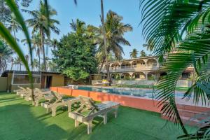 a resort with a pool with benches and palm trees at Rosa Bella Resort-TBV in Calangute
