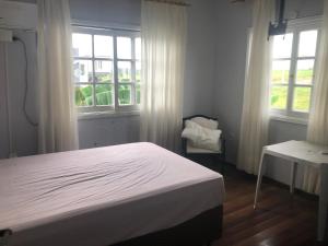 a bedroom with a bed and a table and windows at Pousada Sossego in São Gabriel