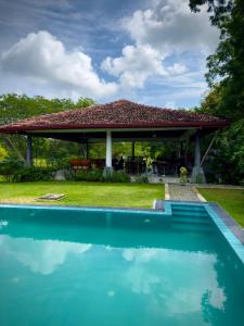 a swimming pool in front of a house with a gazebo at Magalle Wewa Villa in Nikaweratiya