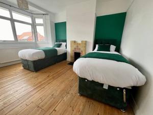 two beds in a room with green walls and wooden floors at Treasure Chest Chessington in Ewell