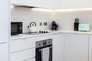 a kitchen with white cabinets and a stove top oven at Modern New 1BR wbalcony, 2min Tottenham Hale Tube in London