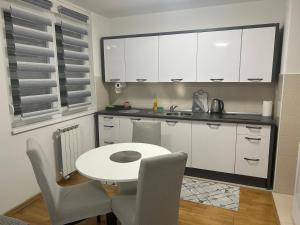 Apartment Mija-Meri في توزلا: مطبخ بدولاب بيضاء وطاولة وكراسي بيضاء