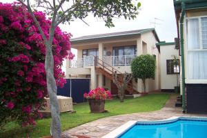a villa with a swimming pool in front of a house at Birdcage B&B in Amanzimtoti