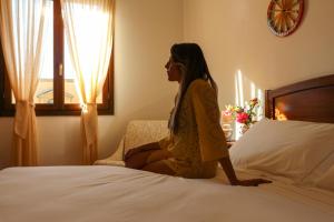 una mujer sentada en una cama en una habitación de hotel en Hotel La Corte Del Sole, en Noto