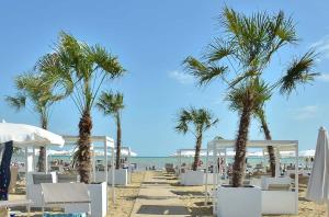 uma praia com cadeiras brancas e palmeiras e o oceano em Lovely beachside flat with a luminous terrace em Bibione