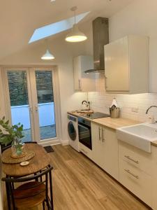 een keuken met witte kasten, een tafel en een wastafel bij The Cottage, Bridge House in Laxey