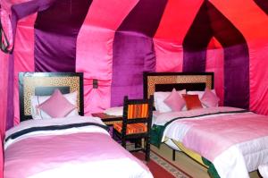 two beds in a pink and purple tent at Rainbow Desert Camp in Merzouga