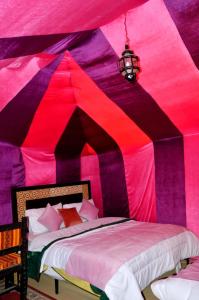 a bedroom with a pink and purple tent with two beds at Rainbow Desert Camp in Merzouga