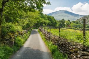 a road with a stone wall and mountains in the background at Sygun Fawr Country House in Beddgelert