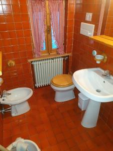 La salle de bains est pourvue de carrelage rouge, de toilettes et d'un lavabo. dans l'établissement Appartamenti Nonno Gianni, à Rocca Pietore