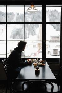 einem Mann, der an einem Tisch vor einem Fenster sitzt in der Unterkunft Ski Lodge Engelberg in Engelberg