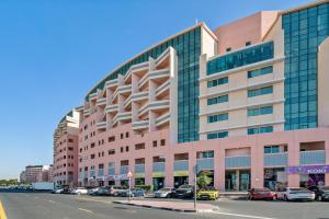 Luxurious Apt Near Jbr في دبي: مبنى وردي كبير مع سيارات تقف في موقف للسيارات