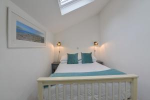 a white bedroom with a bed with blue pillows at Kelmscot in Port Isaac