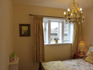 Dormitorio con ventana, cama y lámpara de araña en Wood End Cottage en Slaithwaite