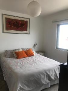 un letto bianco con cuscini arancioni in una camera da letto di Departamentos Quintaviña K15 a Viña del Mar