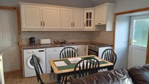 - une cuisine avec des placards blancs, une table et des chaises dans l'établissement Boola Cottage, 
