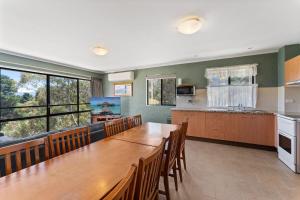 a dining room with a long table and a kitchen at Alpine Mountain View 18 - 4BR l Mountain Views l Swimming Pool l Air-Con l WiFi in Jindabyne