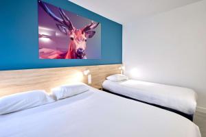 twee bedden in een hotelkamer met een schilderij van een hert bij Kyriad Direct Narbonne Sud in Narbonne