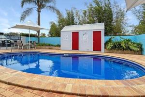 una piscina con un edificio y una sombrilla en 3-Bed with Alfresco Dining & Pool in Batemans Bay, en Batemans Bay