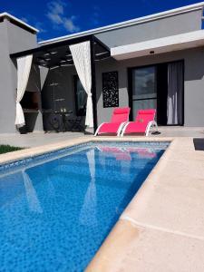 a swimming pool with two pink chairs next to a house at Tres Deseos in Villa Cura Brochero