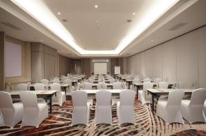 a conference room with tables and white chairs and a screen at HARRIS Hotel & Convention Cibinong City Mall Bogor in Bogor