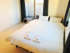 東京にあるアンドステイ島尻5丁目の大きな白いベッドとタオルが2枚置かれた寝室