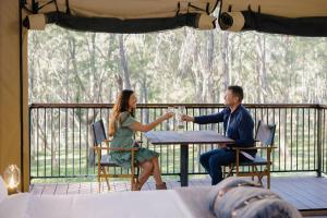 Ein Mann und eine Frau, die mit Getränken am Tisch sitzen. in der Unterkunft Paradise Country Farmstay in Gold Coast