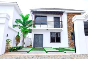 a white house with a black door and a palm tree at Harmony Villa in Tema