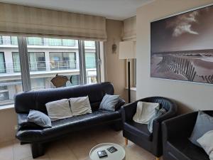 ein Wohnzimmer mit einem schwarzen Ledersofa und Stühlen in der Unterkunft Apartment Gounod Nieuwpoort in Nieuwpoort