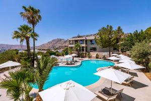 a resort with a pool with umbrellas and palm trees at White Olive Premium Lindos in Pefki