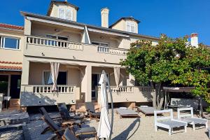 un bâtiment avec des chaises et des parasols en face de celui-ci dans l'établissement Apartments Frankić, à Rab