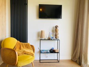 uma sala de estar com uma cadeira amarela e uma televisão em Le Clos de Jade - Appt 3 étoiles avec piscine partagée em Pornic