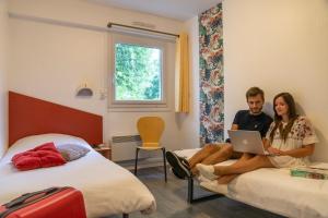 a man and woman sitting on beds with a laptop at Ethic Etapes Lac De Maine in Angers