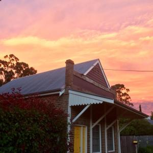 a house with a roof with a sunset in the background at Bundanoon Bijou Southern Highlands Accommodation in Bundanoon