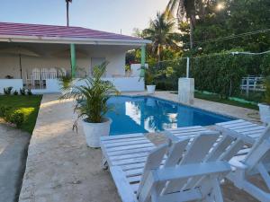 una piscina con 2 tumbonas blancas junto a una casa en Villa sonia, en Juan Barón