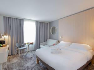 Habitación de hotel con cama blanca grande y escritorio. en Novotel Aix-en-Provence Pont de L'Arc, en Aix-en-Provence